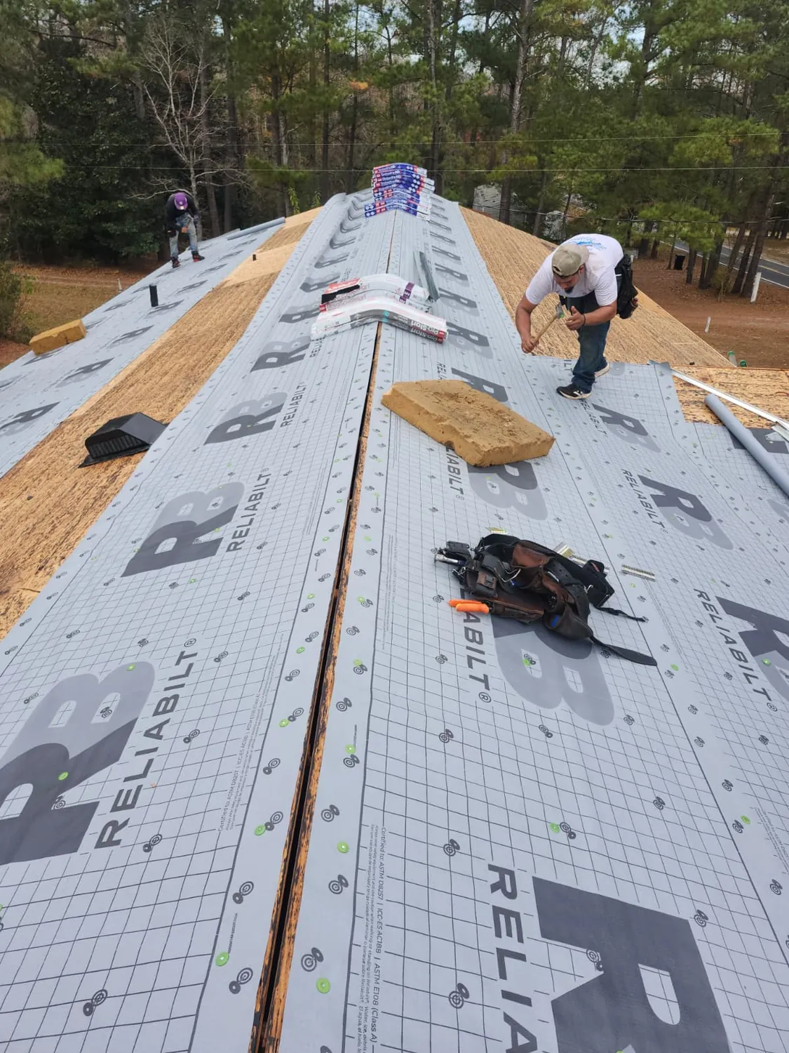 Crew rolling synthetic underlayment up a bare roof deck